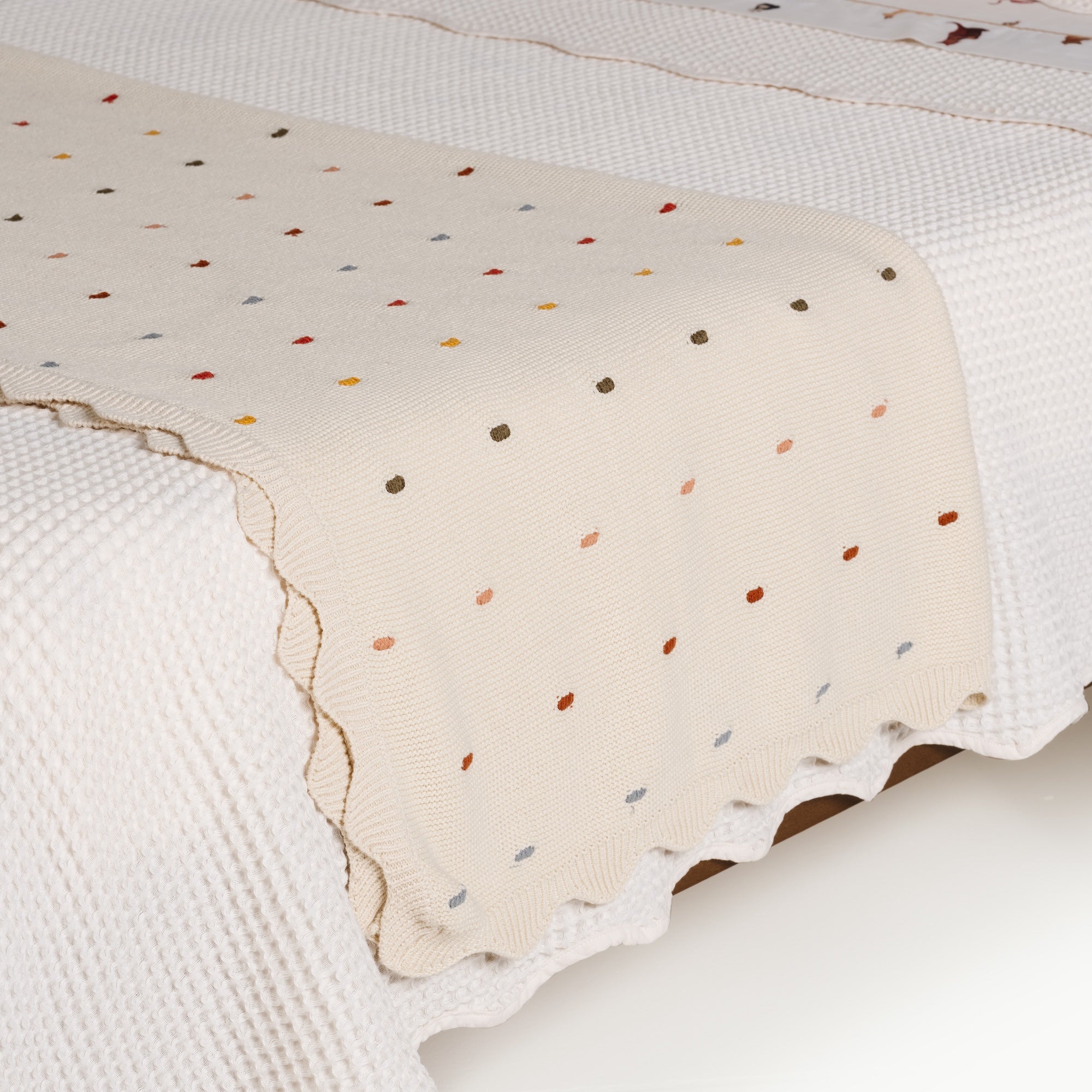 Ivory@Scalloped cotton throw draped across a bed 