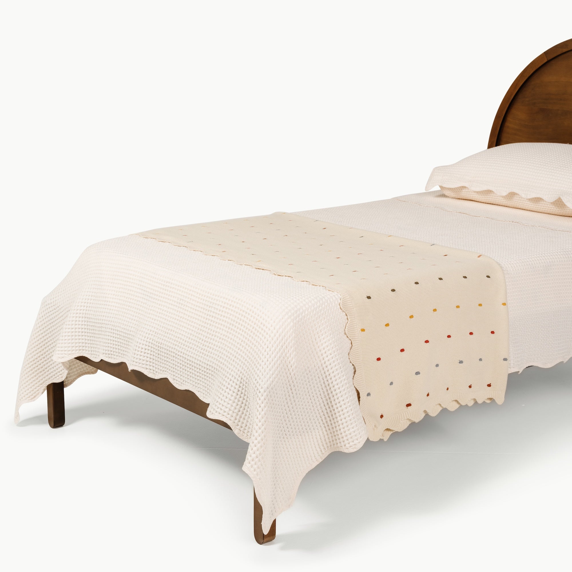 Ivory@Scalloped cotton throw draped across a bed 